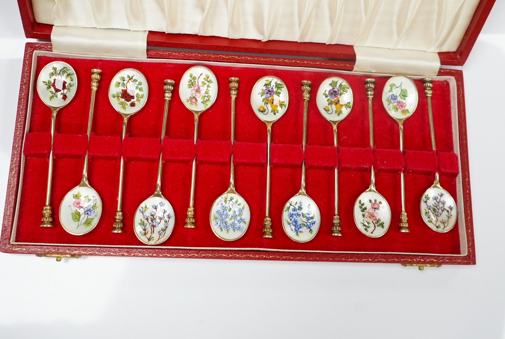 A cased set of twelve early 1970's silver gilt and enamel coffee spoons, decorated with flowers, S.J. Rose & Son, Birmingham, 1971, 98mm. Condition - fair to good